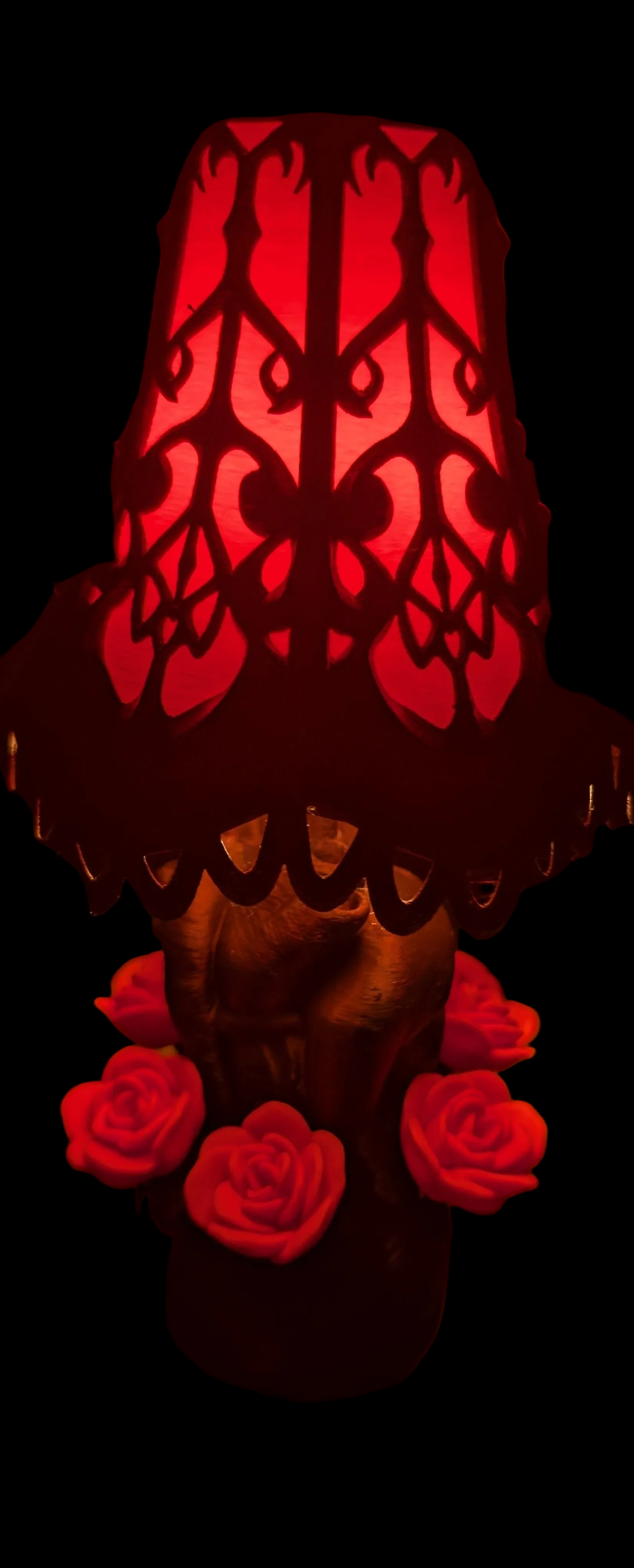 Decorative lamp with red floral base and patterned shade on a black background